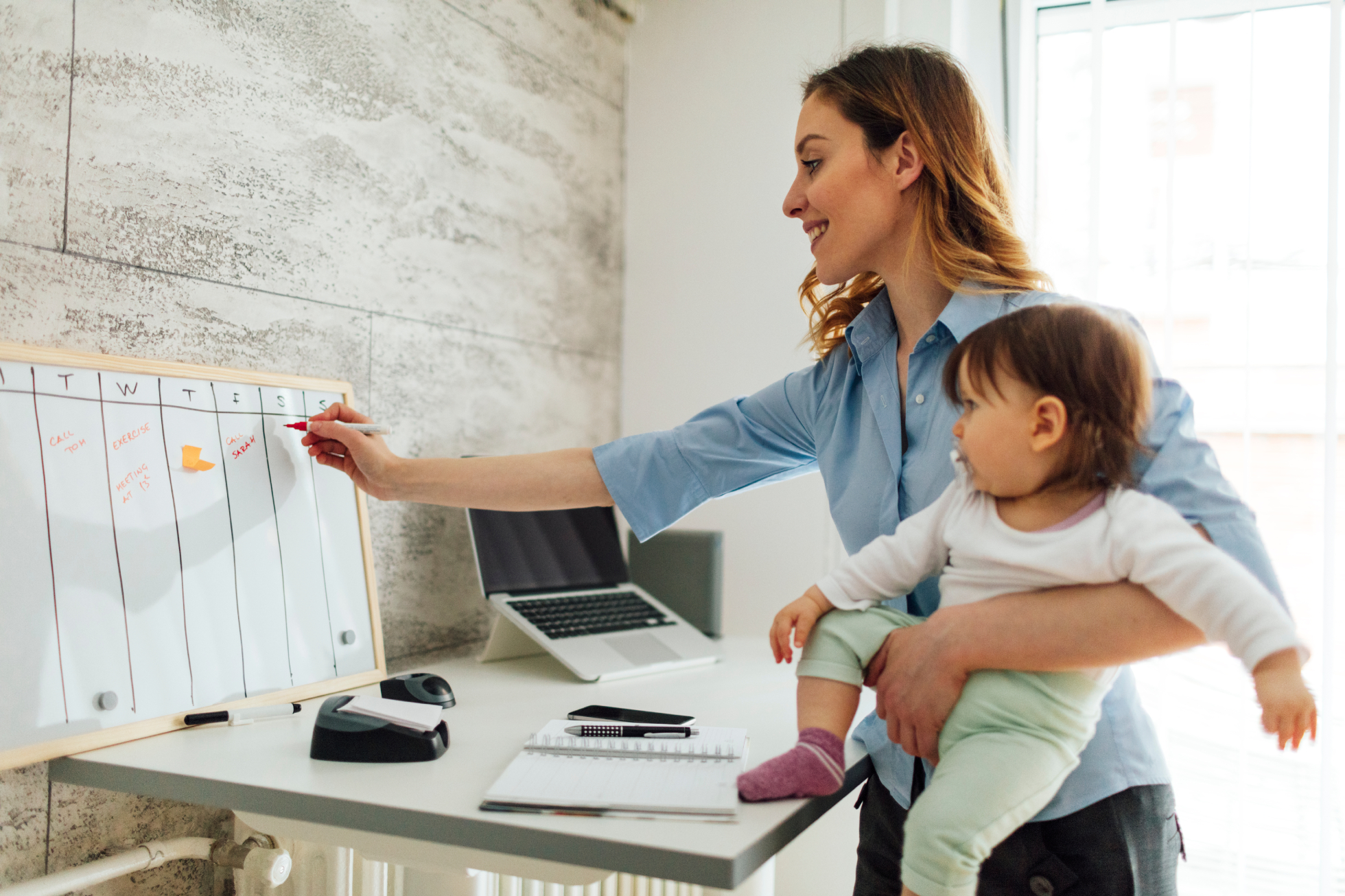 A mother holding a baby and writing on a whiteboard